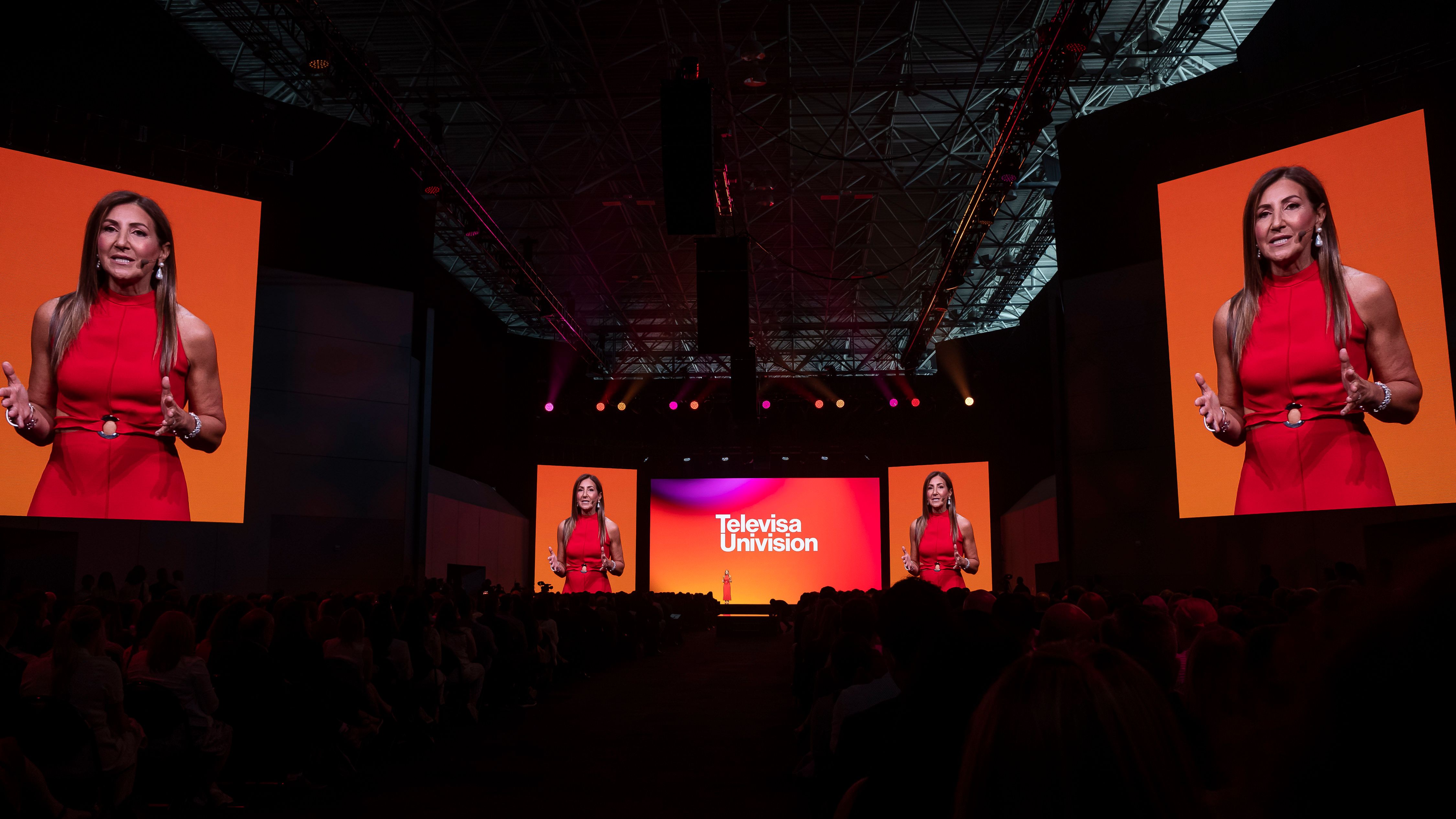 Executive in red presenting on the TelevisaUnivision Upfront stage flanked by giant screens
