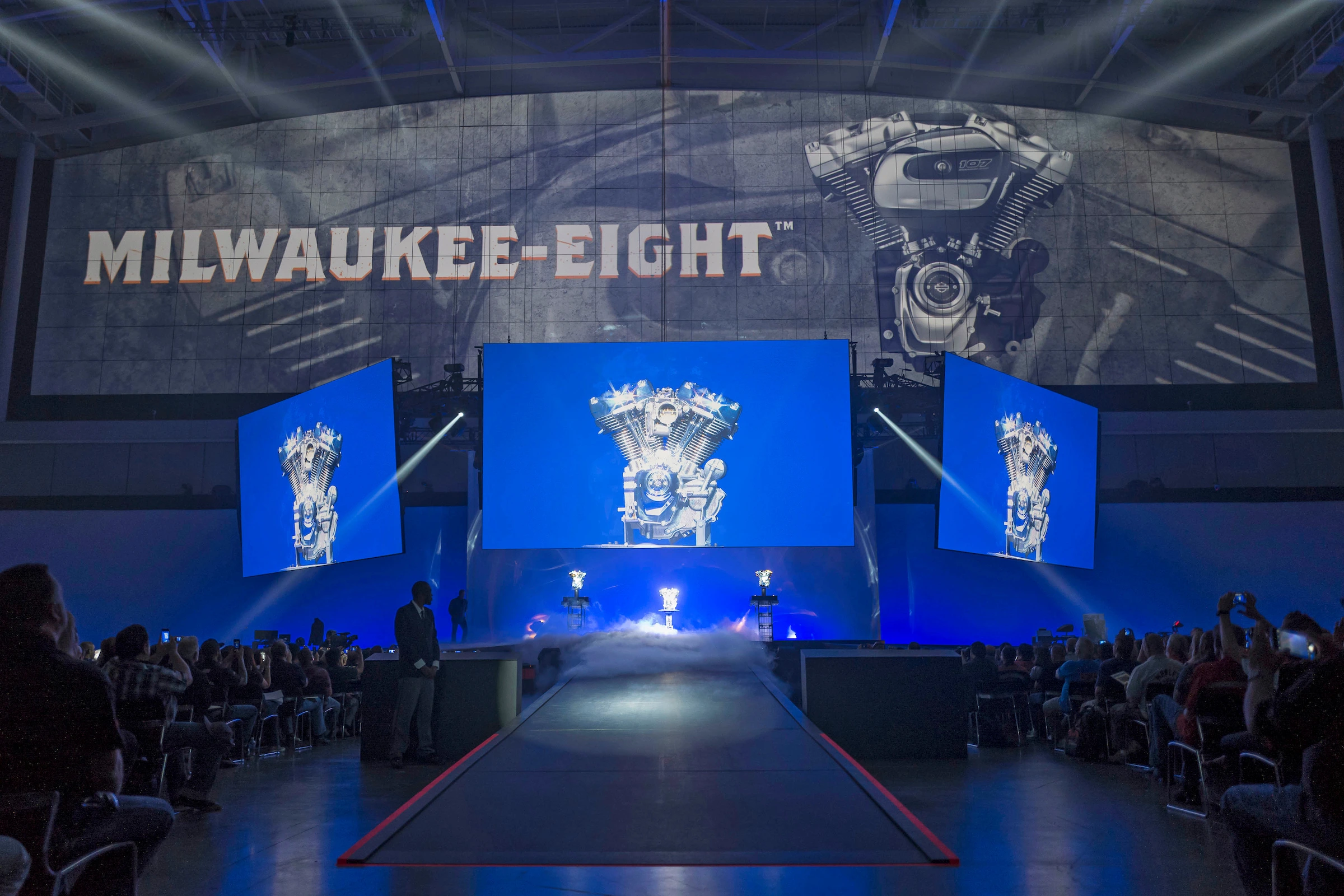 Milwaukee-Eight engine reveal on triple screens over a runway at the Harley-Davidson dealer meeting