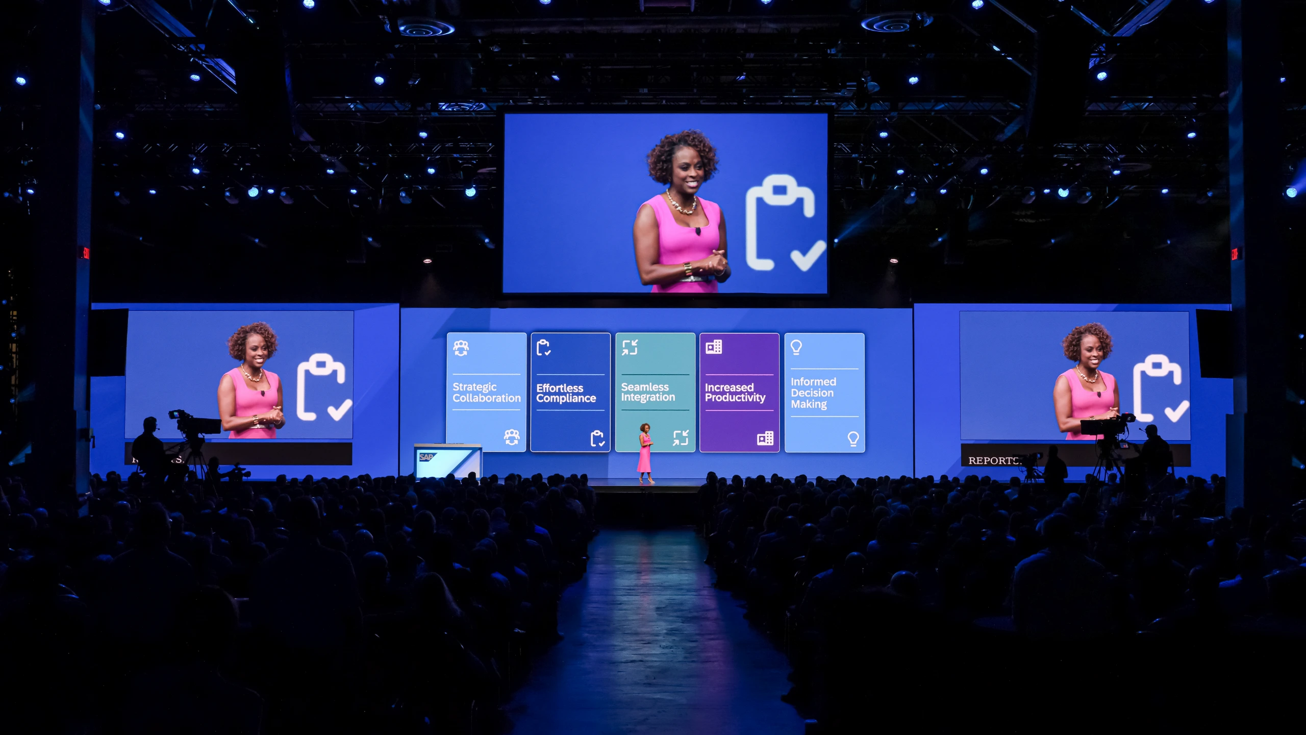 Speaker in pink on the SAP Spend Connect Live 2024 stage with benefit cards on the screens
