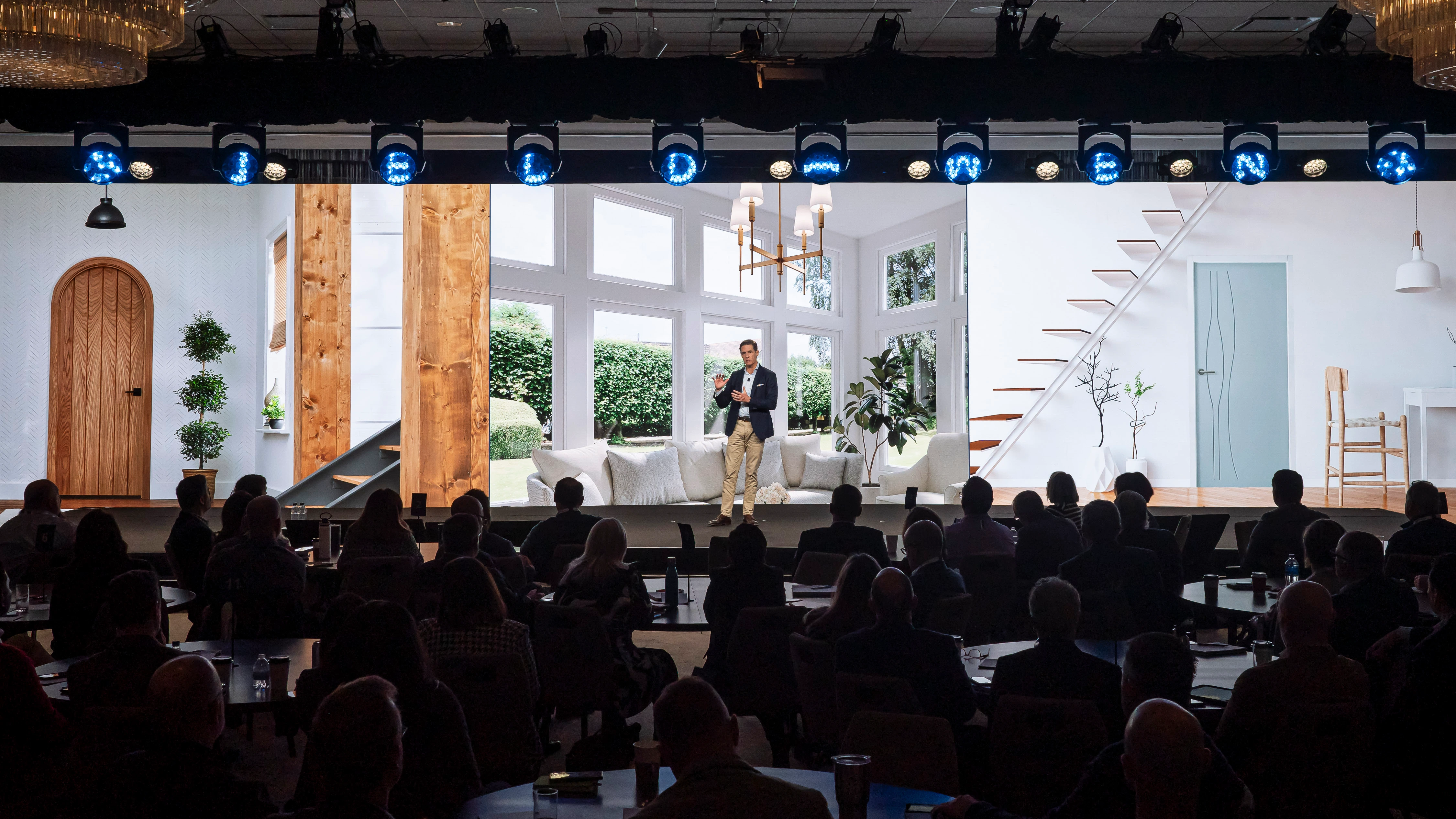 Speaker on the JELD-WEN GLC 2024 stage set styled as a bright home interior, audience at tables