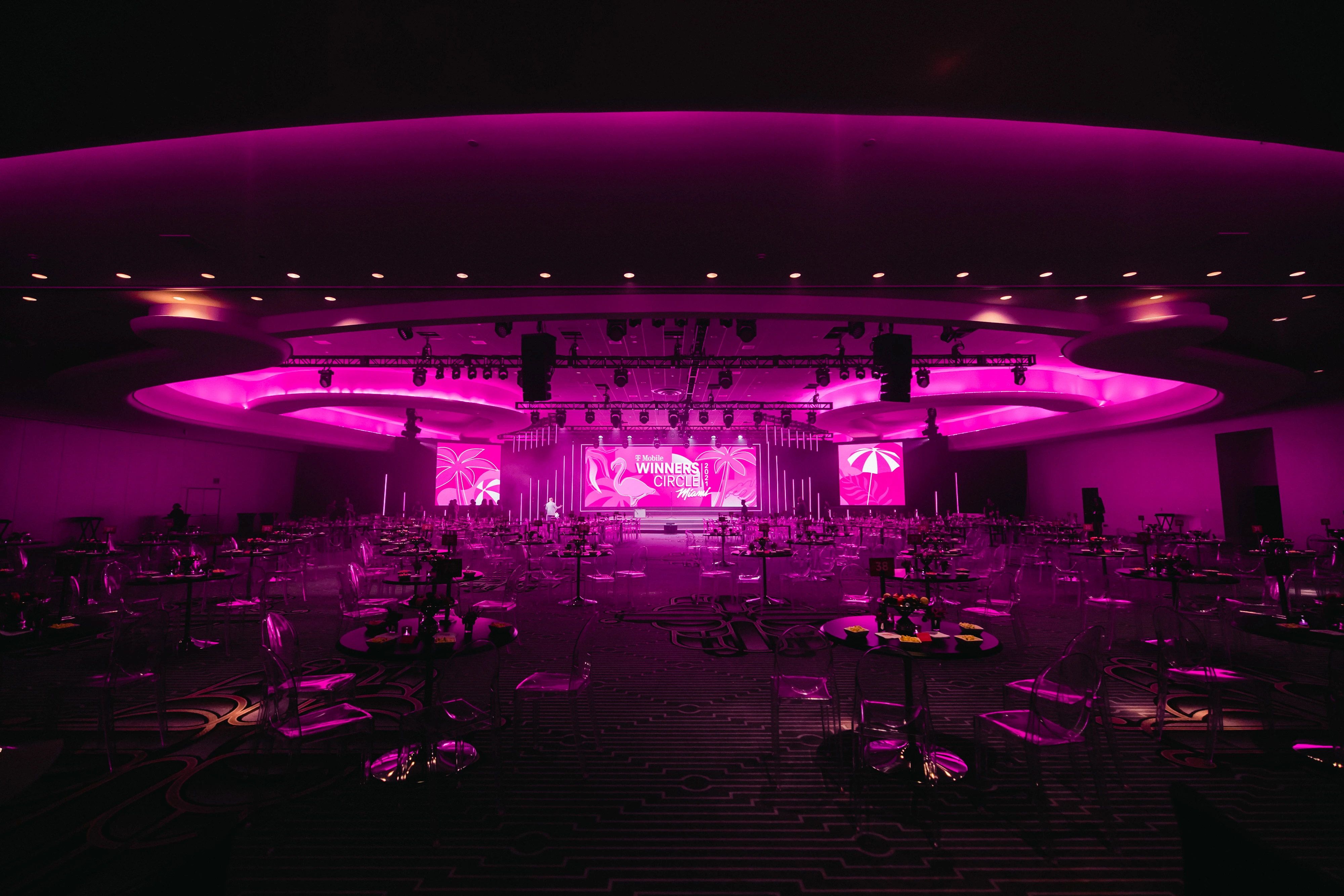 Wide view of the pink-lit Winners Circle Miami ballroom with ghost chairs facing the stage