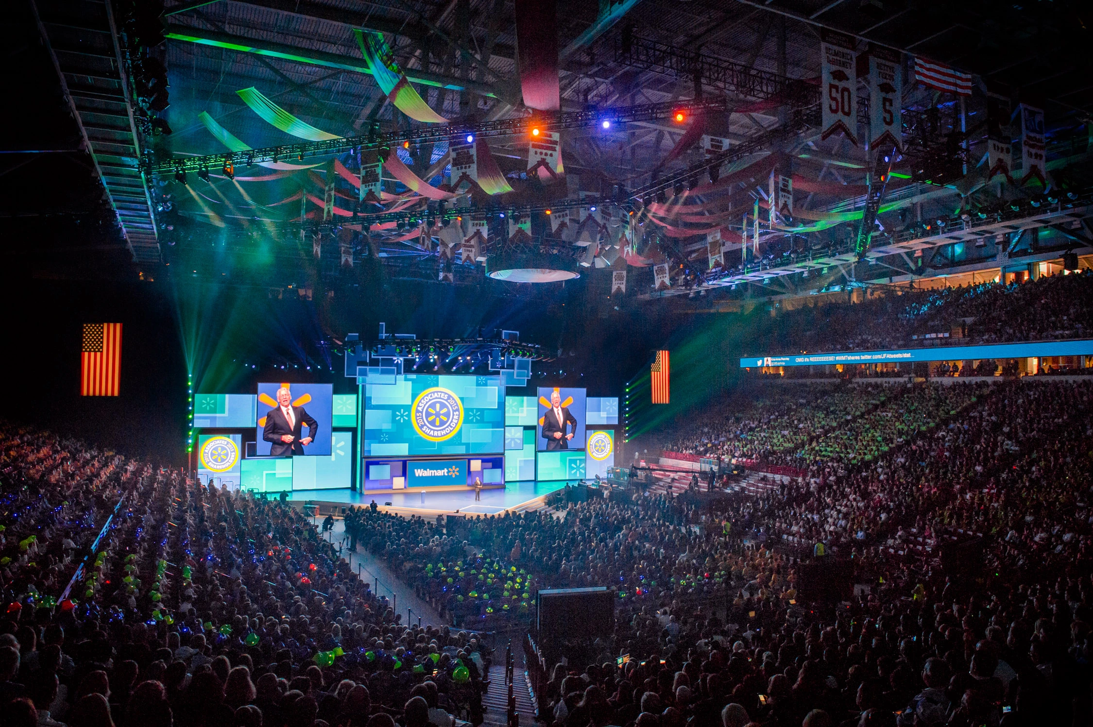 Arena-wide view of the Walmart Shareholders 2015 stage with festive rigging and a keynote speaker on screen